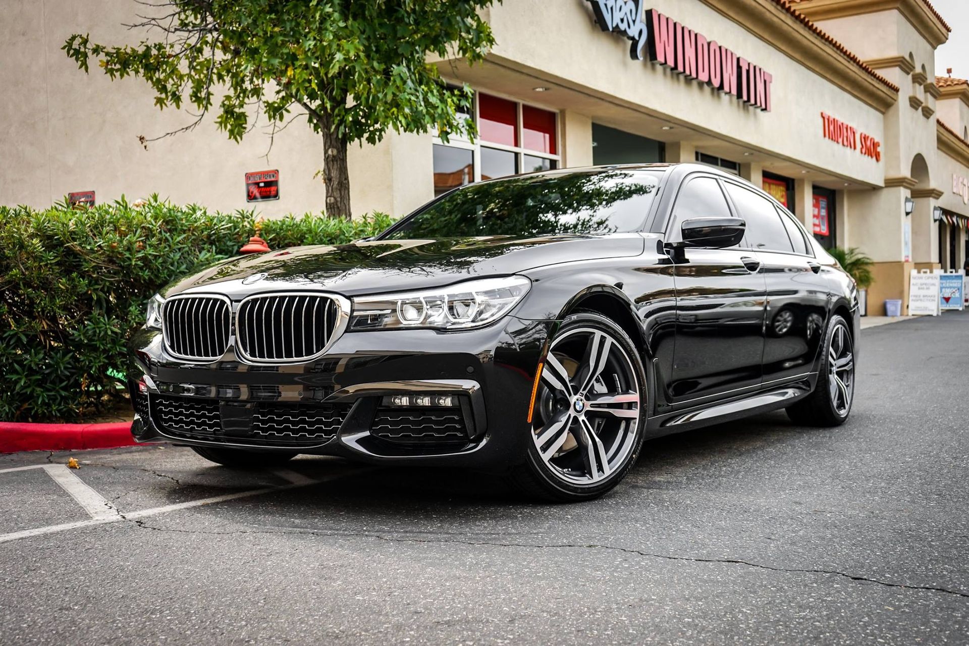 Black BMW sedan parked in front of a shopping center, with trees and shrubs.