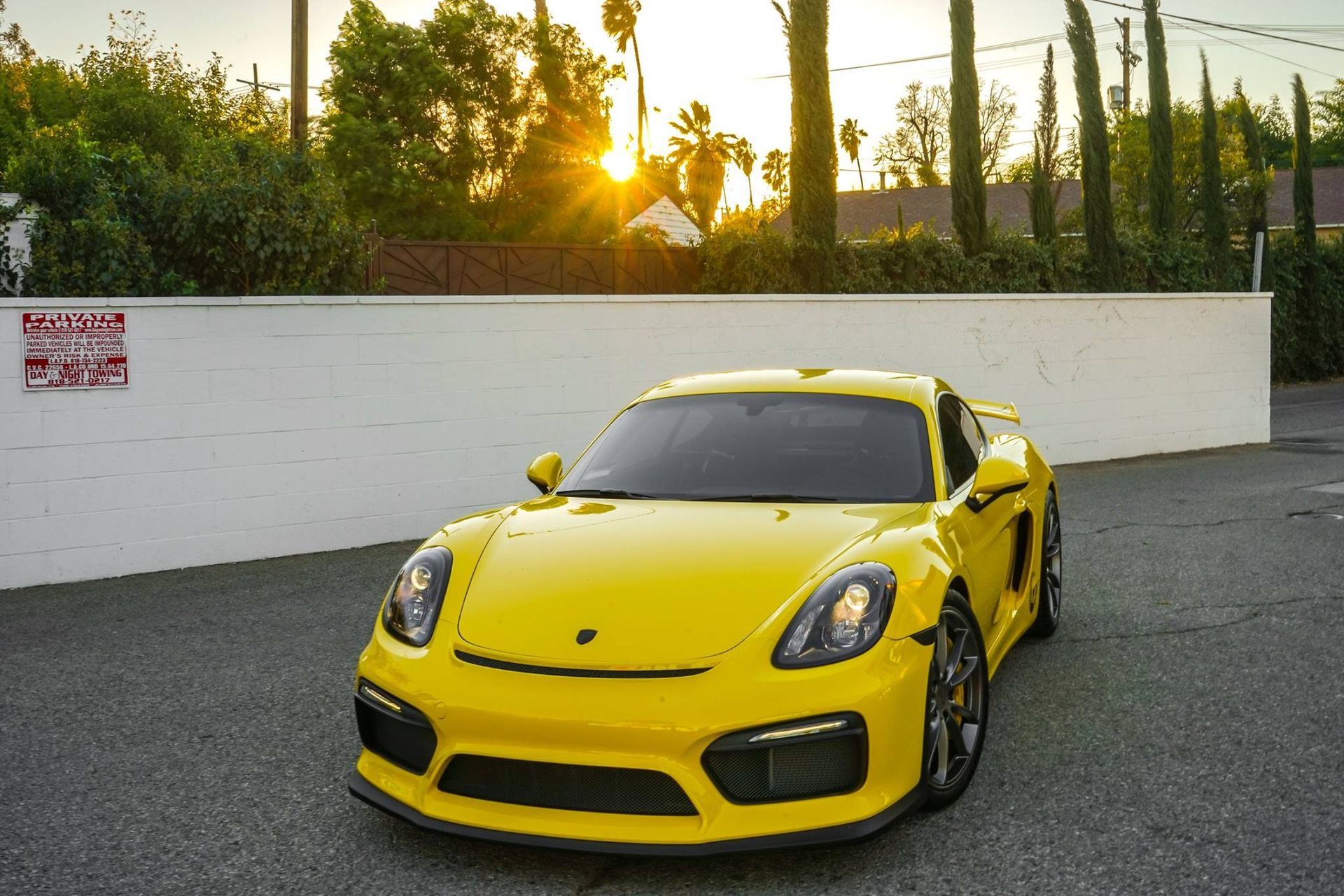 Yellow Porsche sports car parked in front of a white wall, with a sunset in the background.