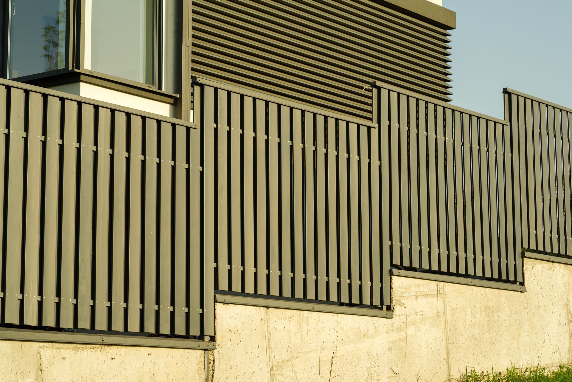 Modern house exterior with vertical slat fence and beige concrete wall in sunlight