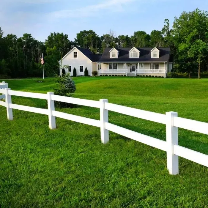 White fence in a green lawn leading to a large white house with a porch and dormer windows.