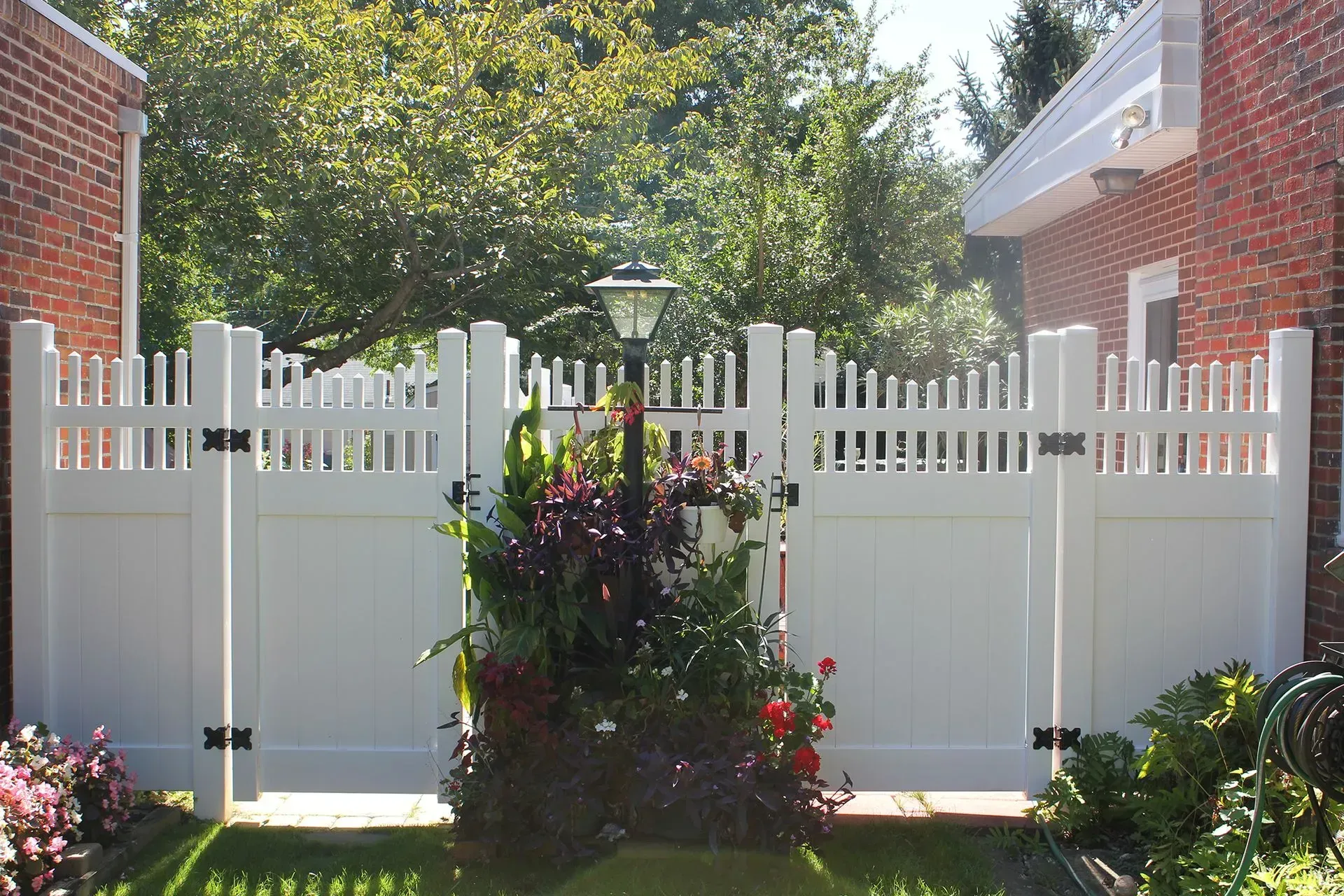 White picket fence with flowering shrub in a sunlit garden courtyard between brick buildings