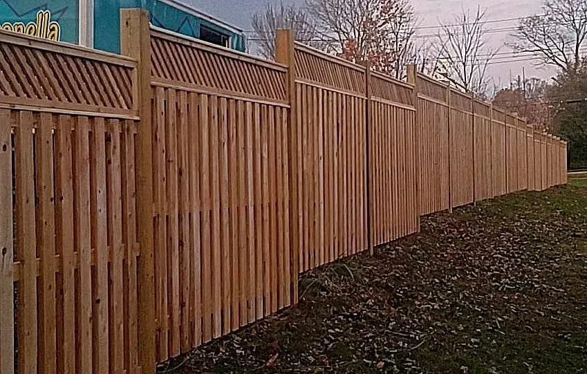 Long wooden fence along a sloped yard beside a sidewalk at dusk