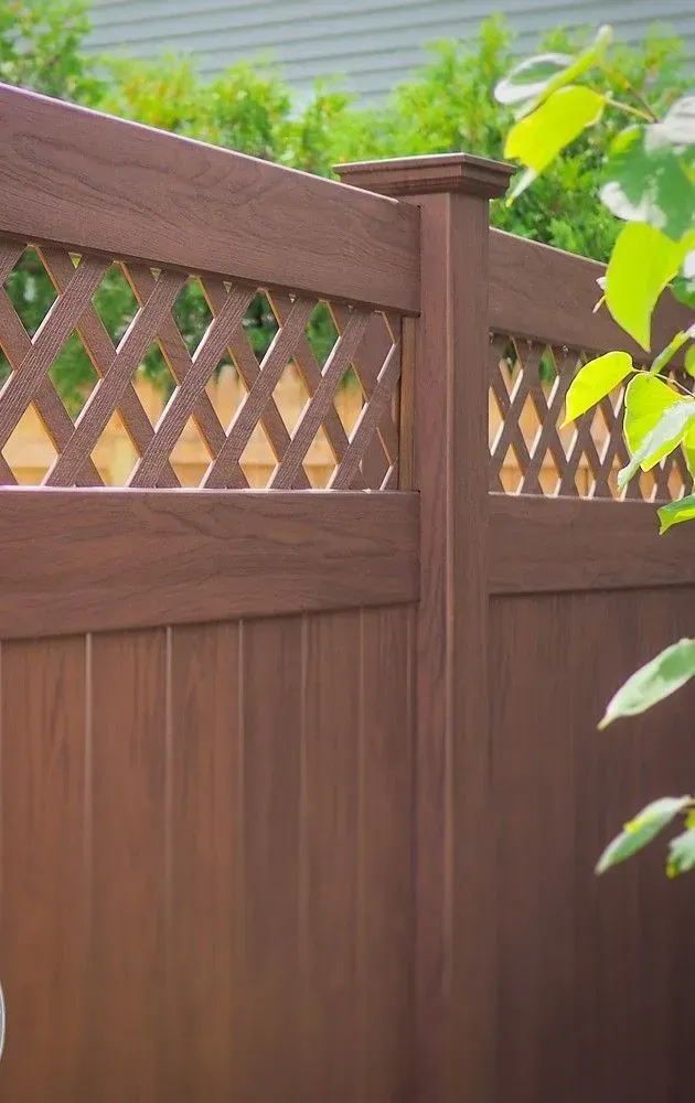 Brown wooden fence with lattice top in a leafy backyard area