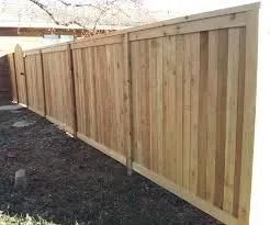 Wooden privacy fence along a gravel yard with a sloped top and white posts