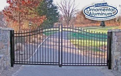 Black wrought iron driveway gate between stone pillars, with Ornamental Aluminum sign in the upper right.