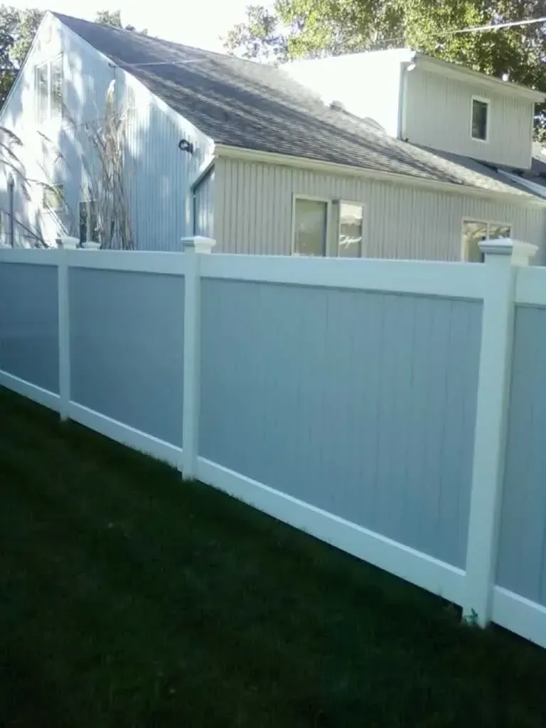 White vinyl fence along a grassy yard beside a light-colored house in bright sunlight