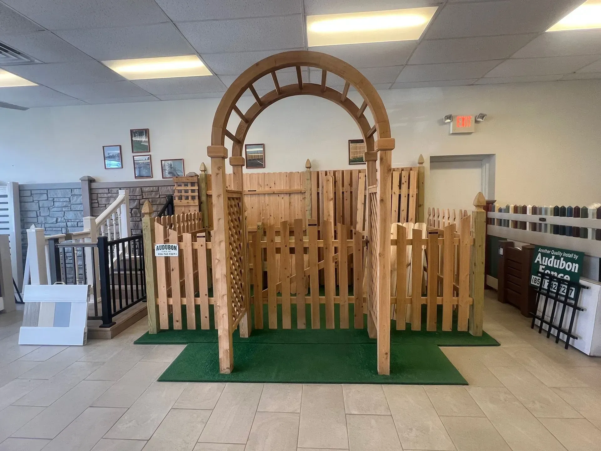 Wooden arch and fence display on green carpet in an indoor retail store, with stairs and racks nearby