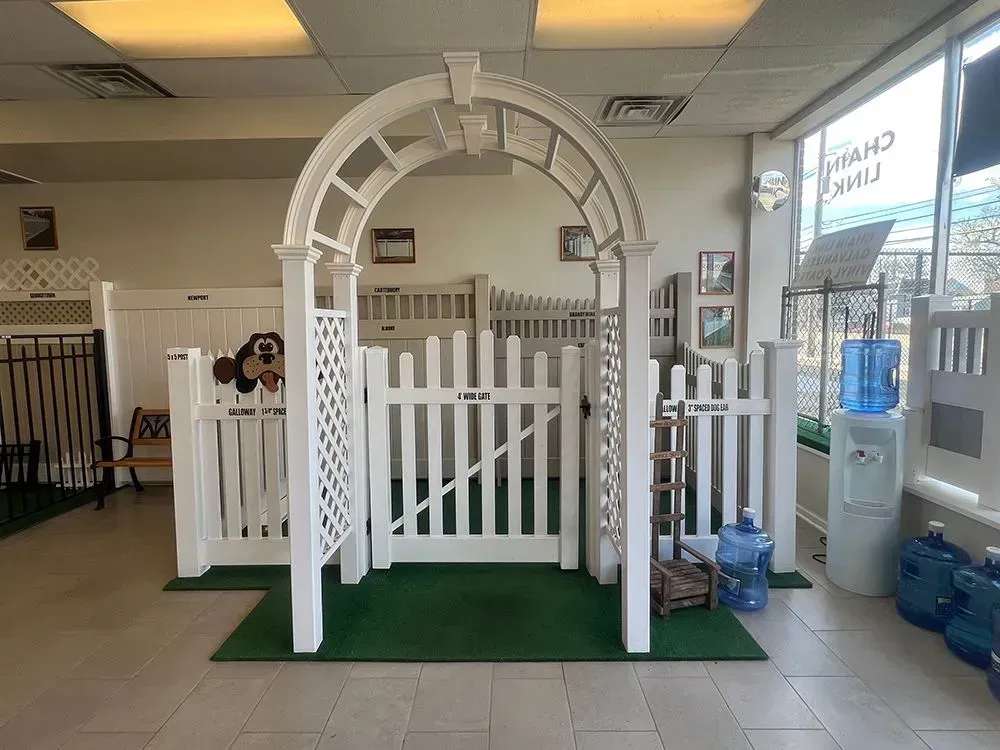 White decorative garden arch and picket fence display on green carpet inside a store.