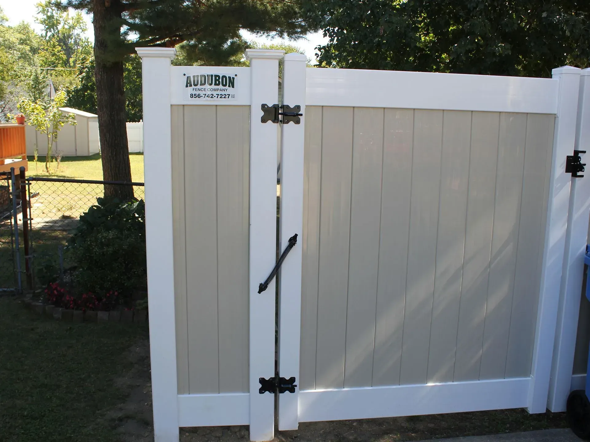 White wooden garden gate with black hinges and latch beside a grassy yard, with a white fence in the background