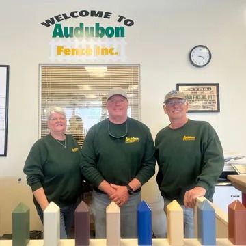 Three staff in green sweatshirts stand behind a counter in an Audubon Fence, Inc. office.