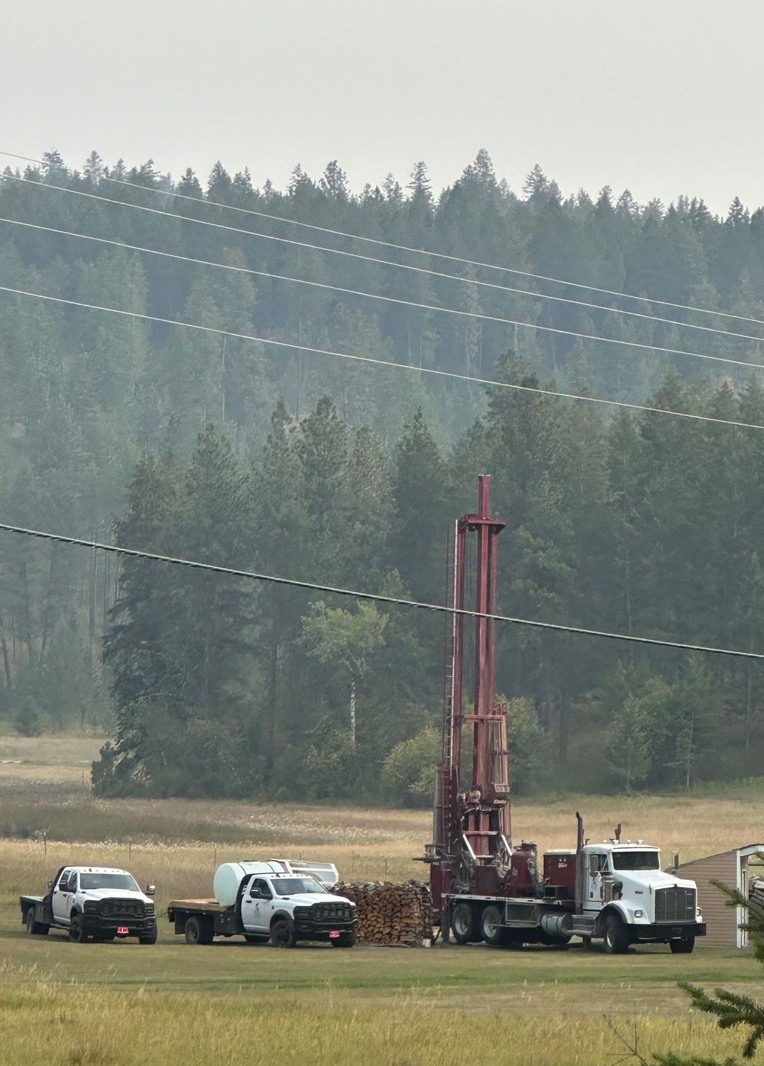 Red well-drilling rig on a truck in a grassy yard with trees in the background.