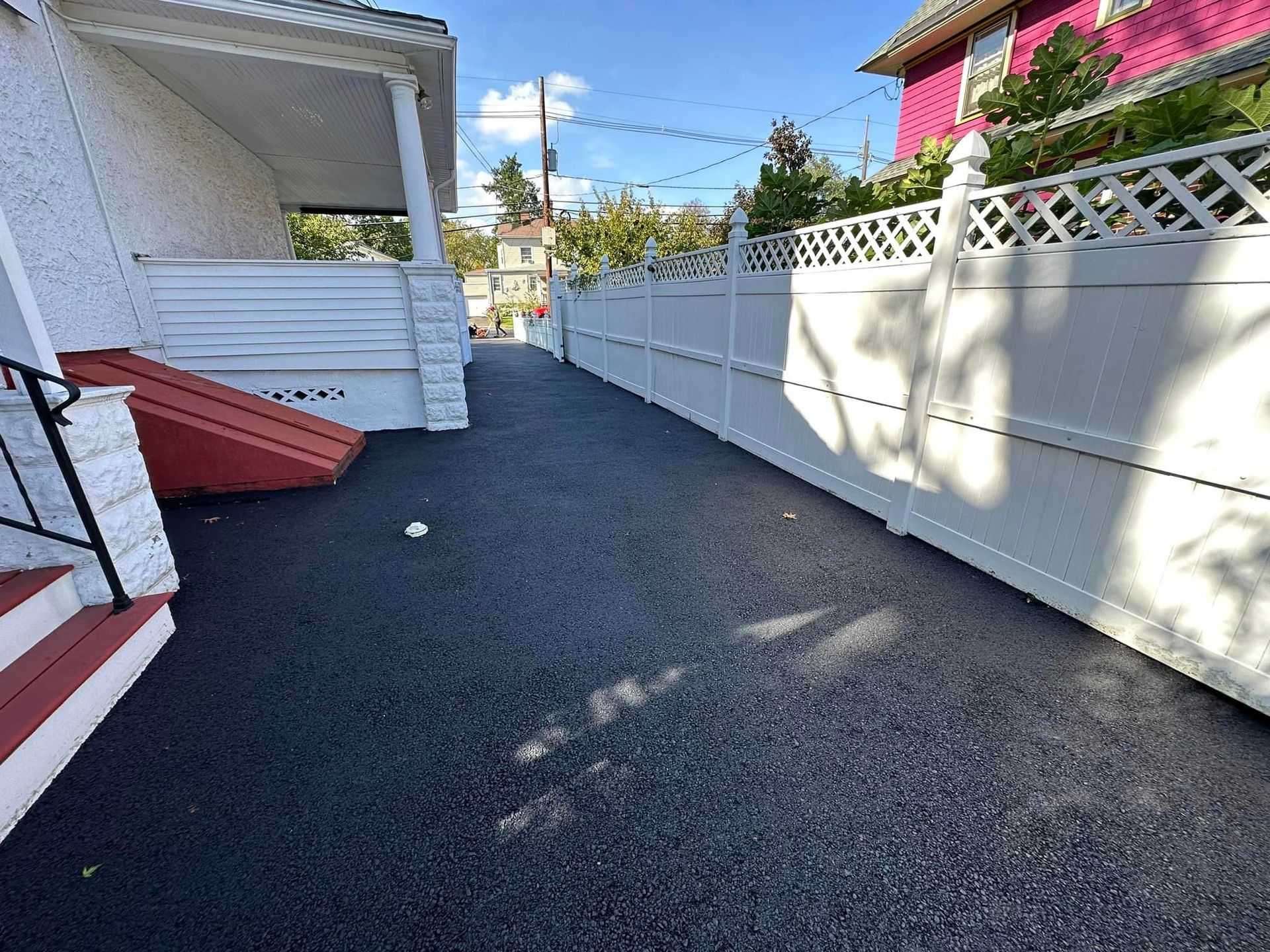A white fence surrounds a driveway leading to a pink house.