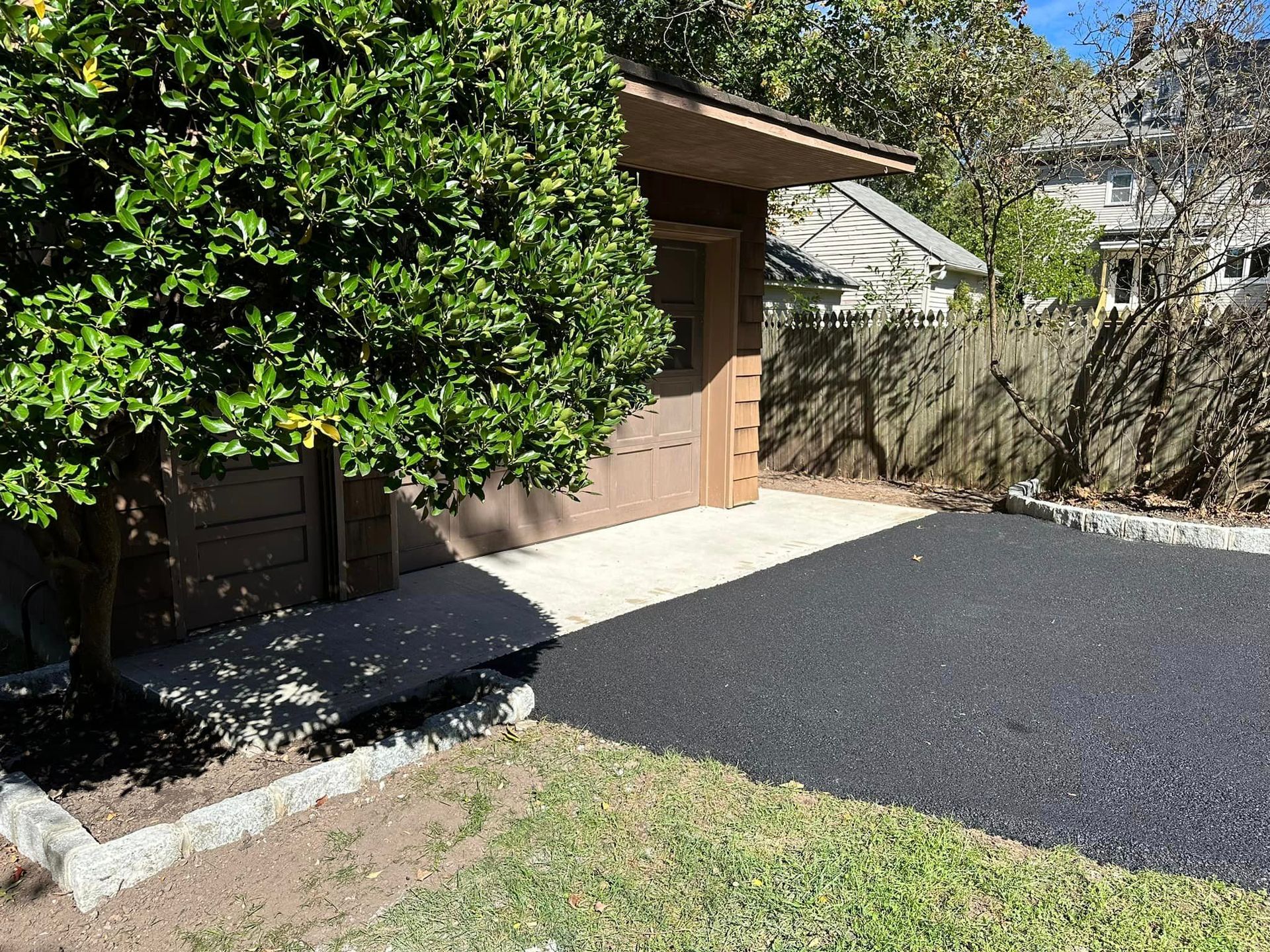 A garage with a driveway and a tree in front of it.