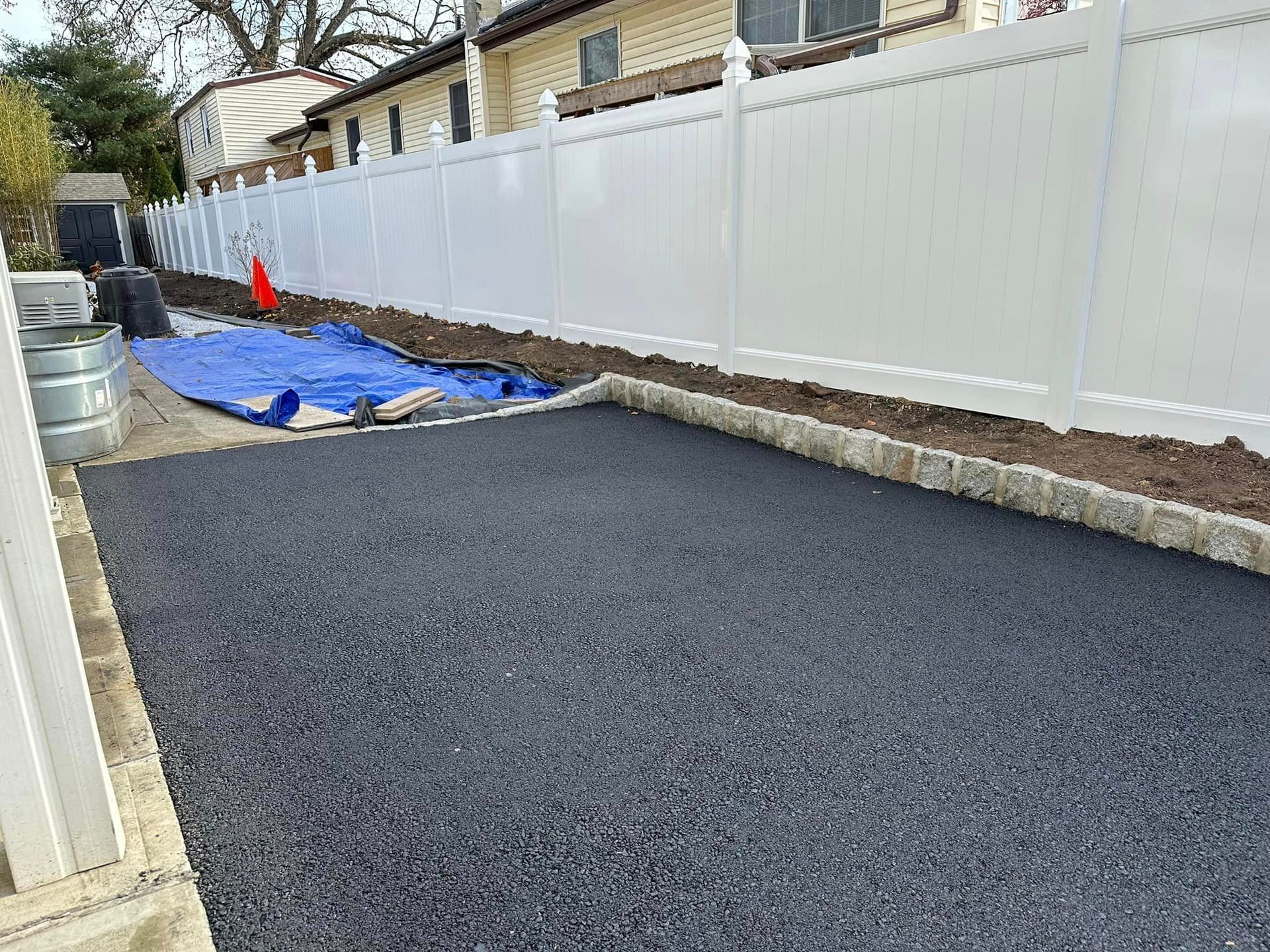 A black asphalt driveway with a white fence in the background.