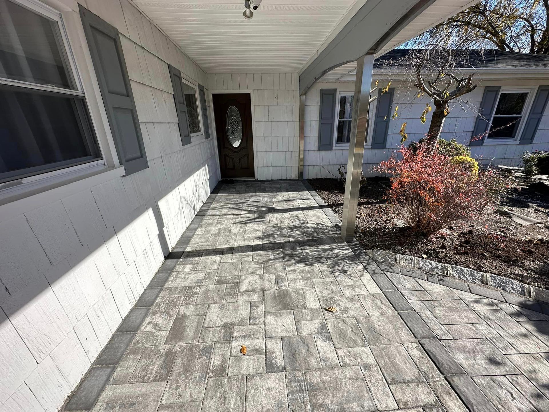 A covered porch with a brick walkway leading to the front door of a house.