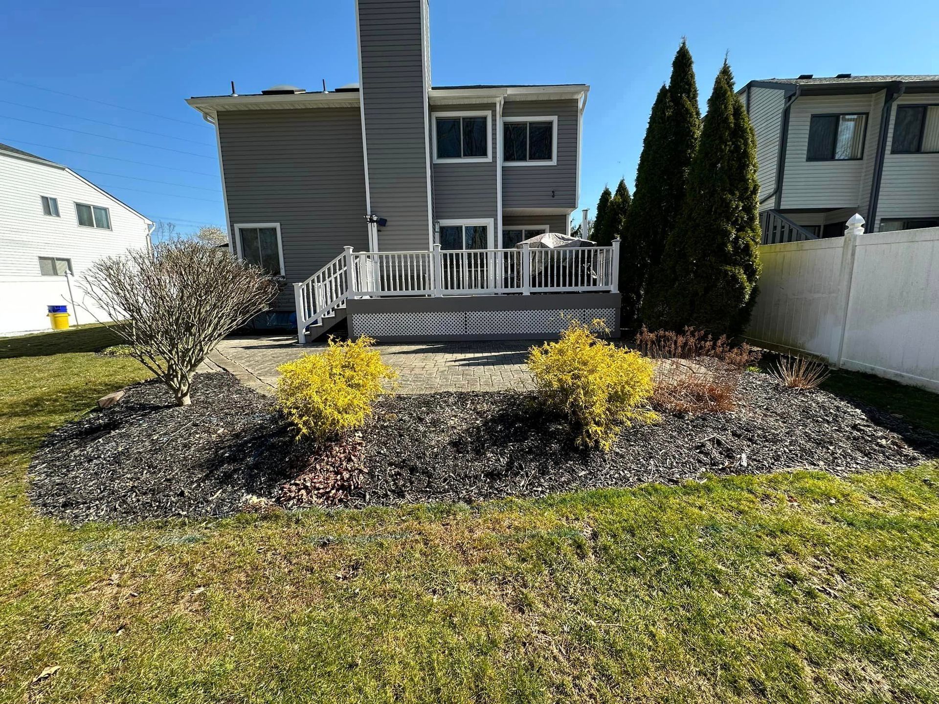 The back of a house with a deck and a white fence.
