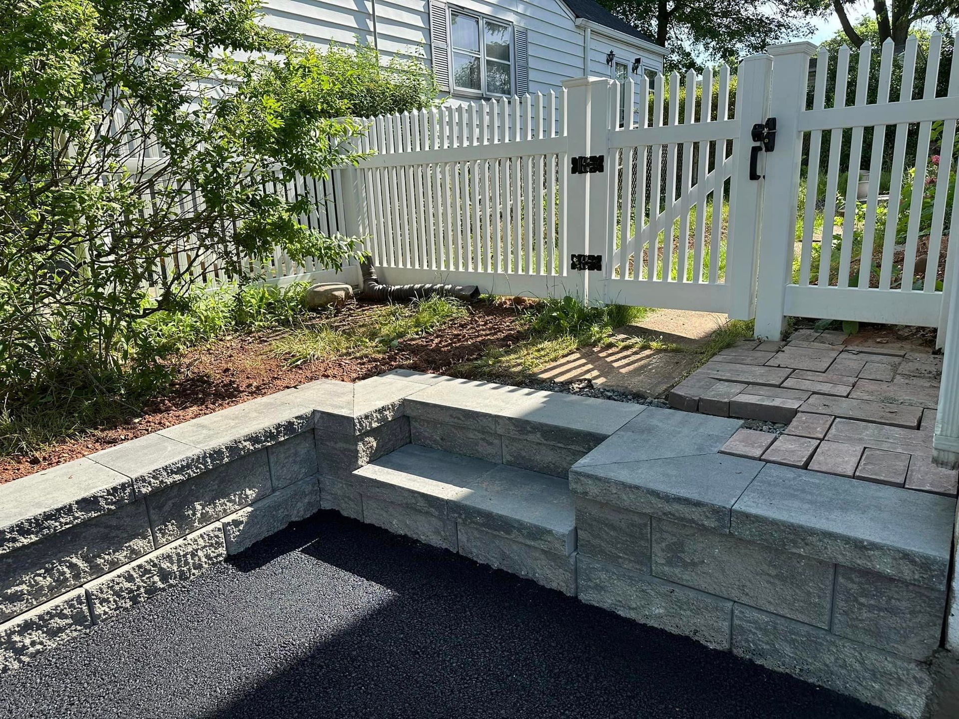 A white picket fence is surrounded by a stone wall and steps.