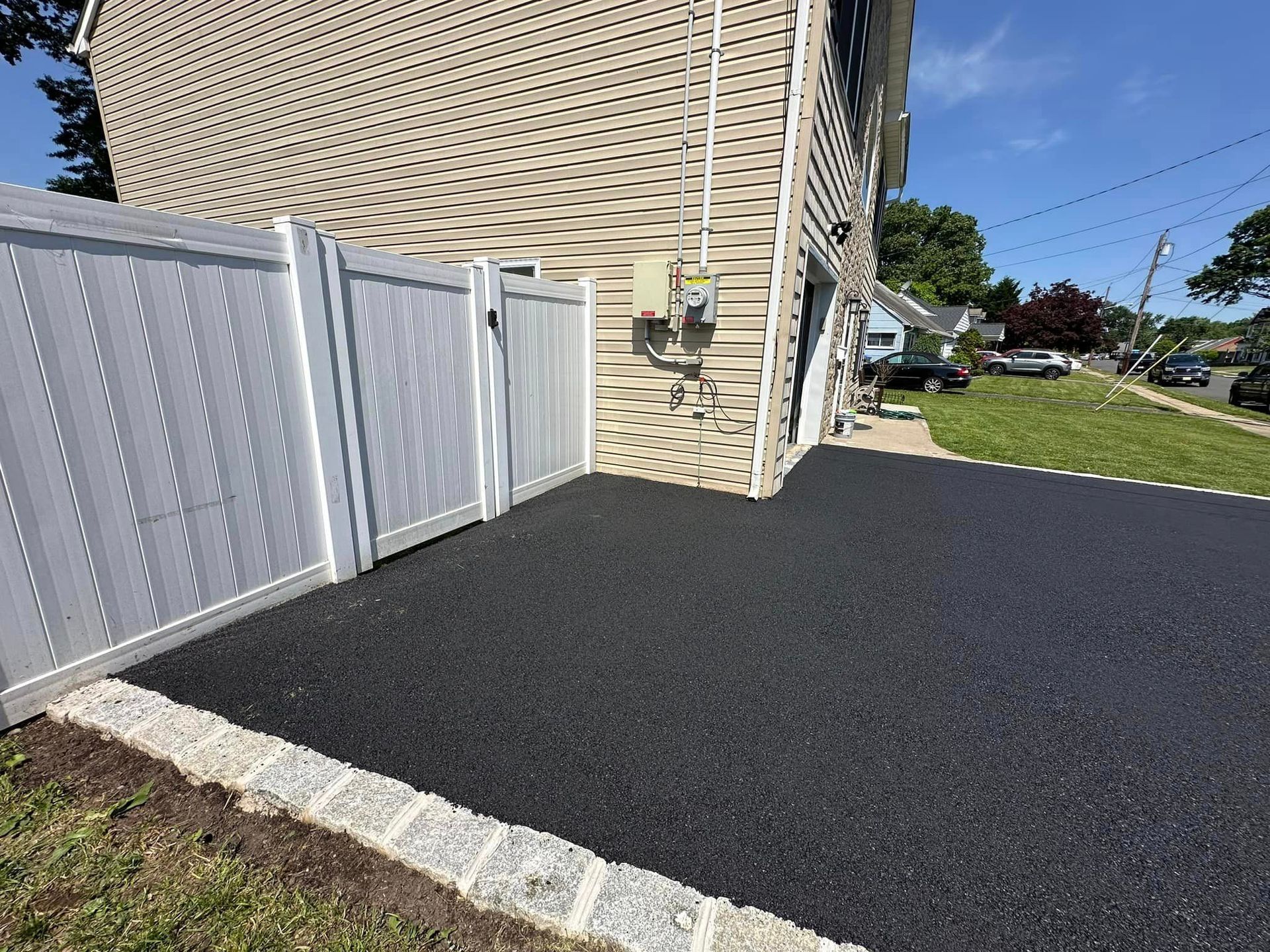 A house with a white fence and a black driveway in front of it.