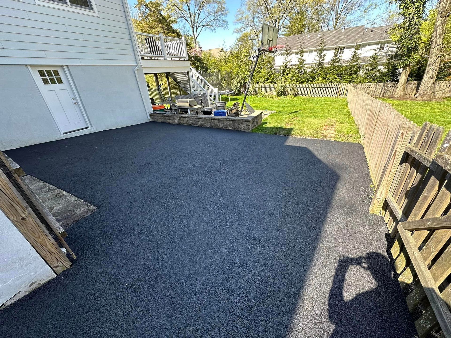 A shadow of a person is cast on a black asphalt driveway in front of a house.