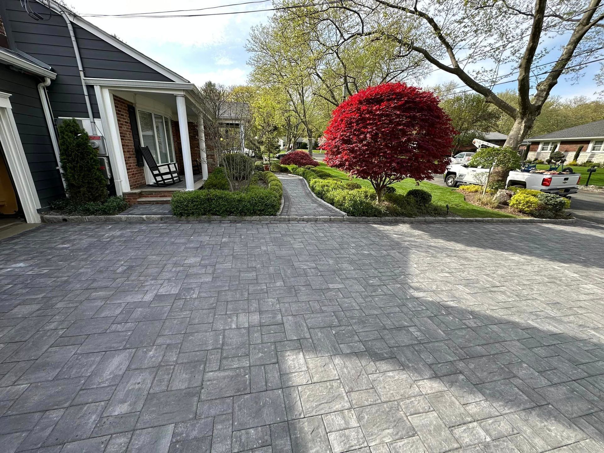 A brick driveway leading to a house with a white truck parked in front of it.