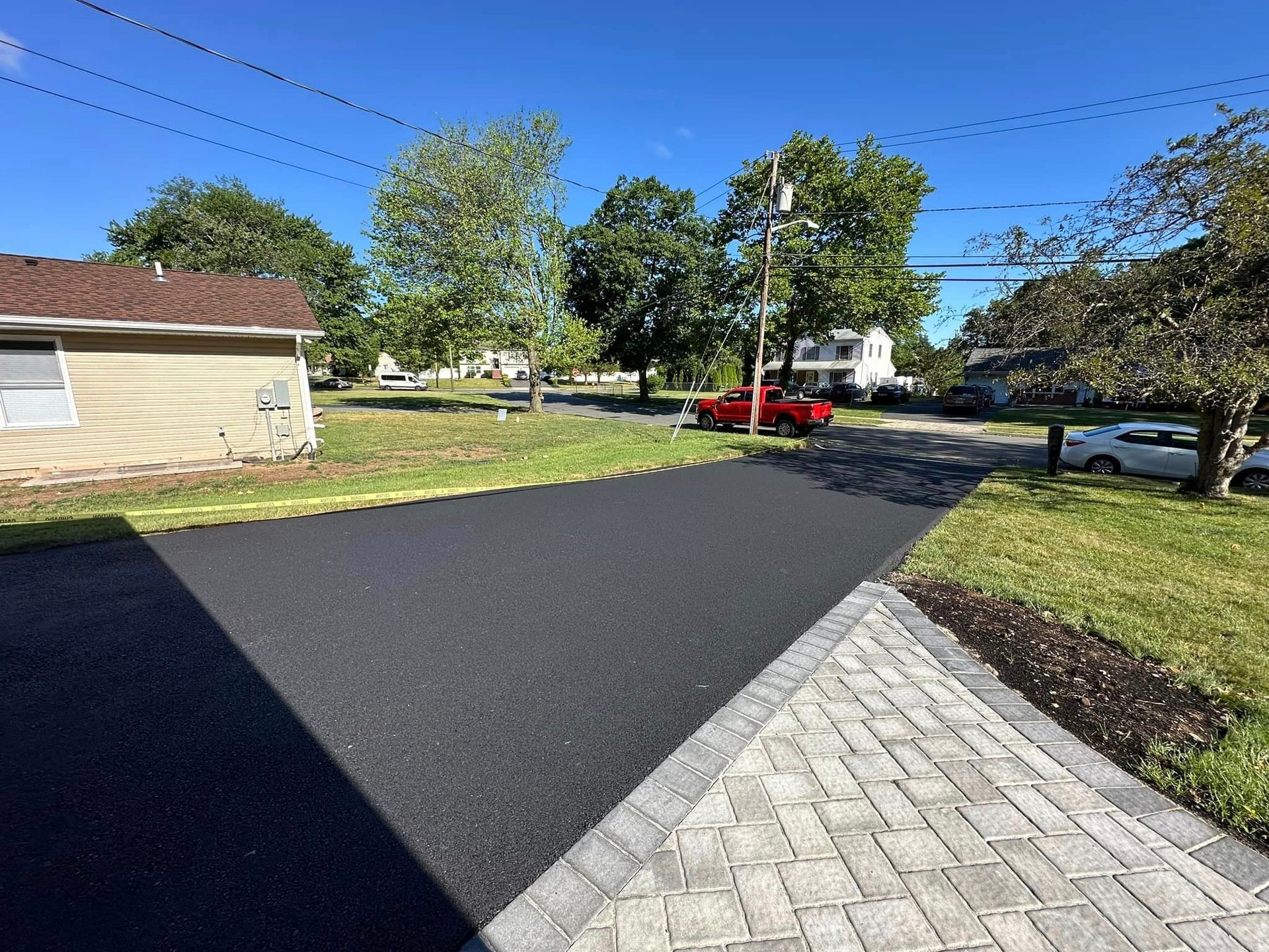 A red car is parked on the side of the road next to a house.
