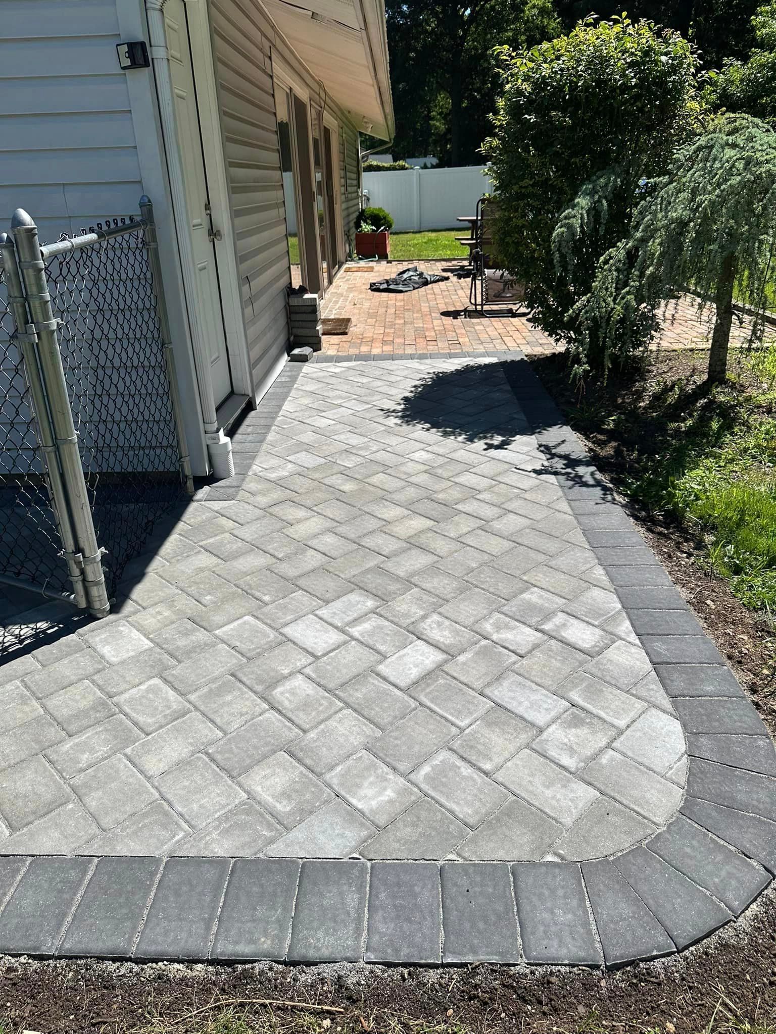A brick walkway leading to a patio next to a house.