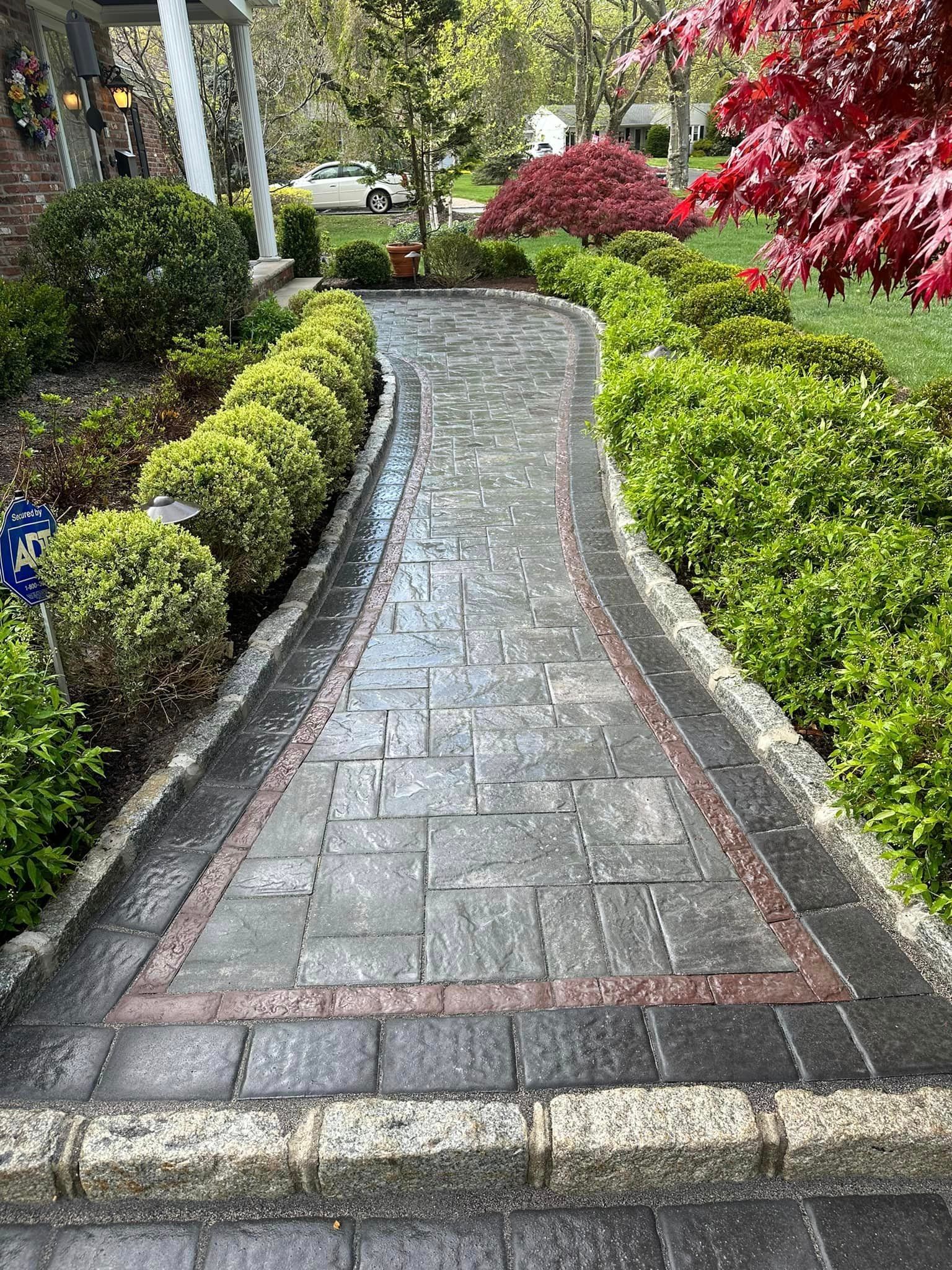 A brick walkway leading to a house surrounded by bushes and trees.