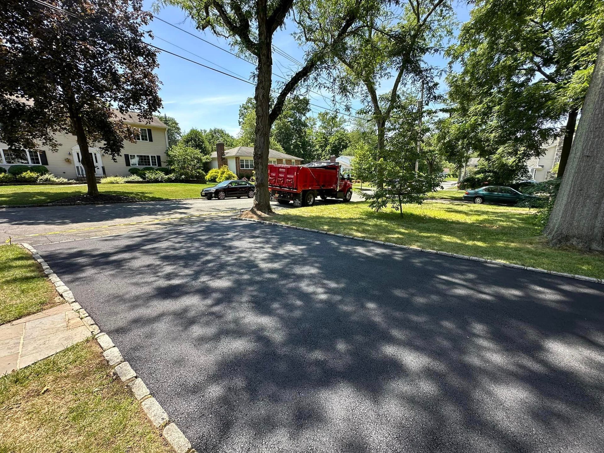 A red truck is parked on the side of a road next to a tree.