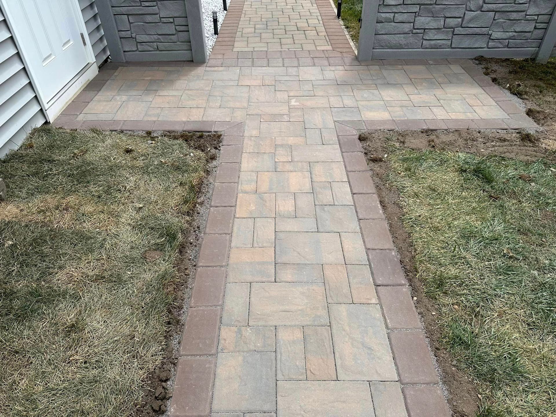 A brick walkway leading to a house with grass on the side.