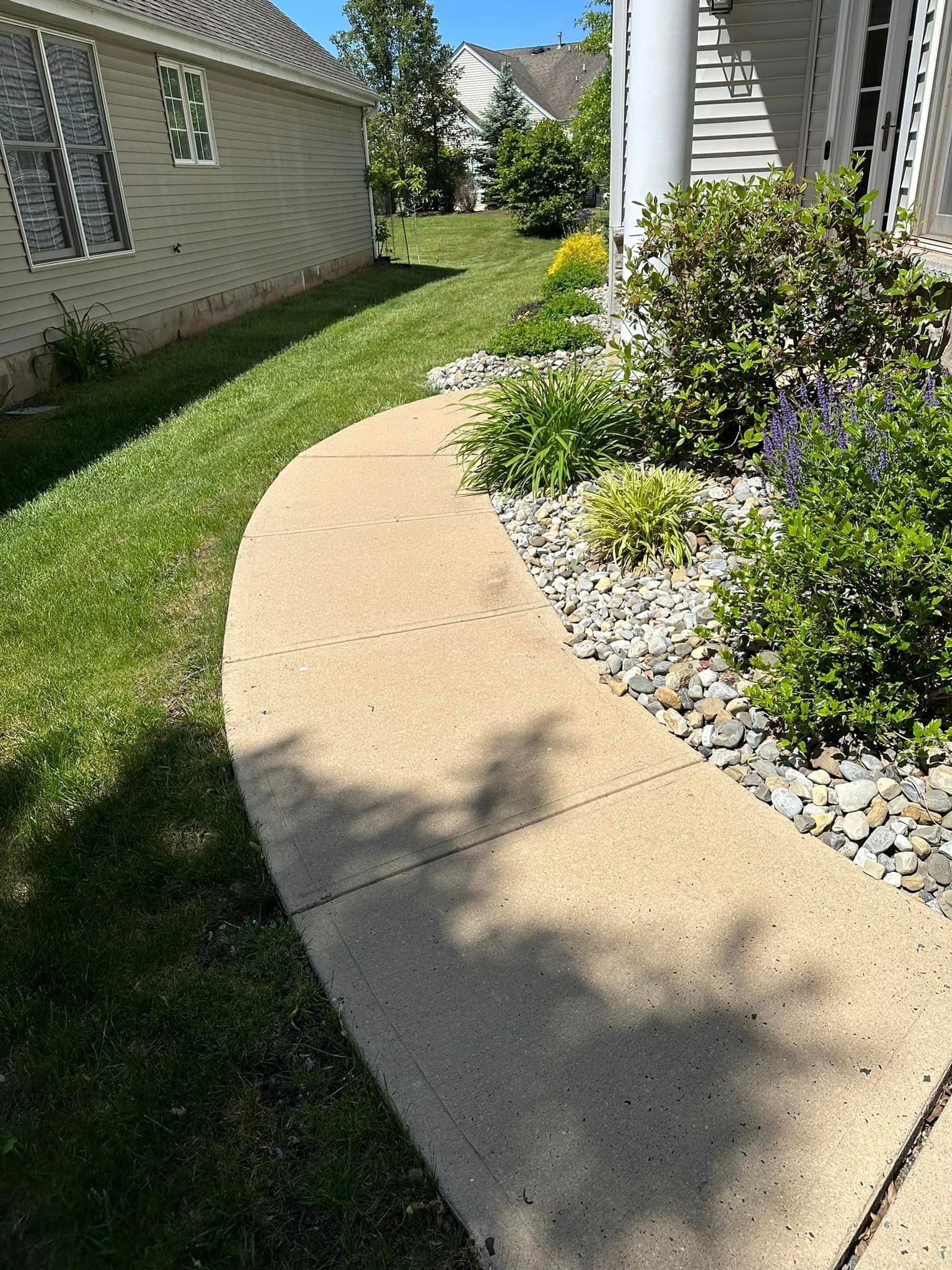 A sidewalk leading to a house with a lot of grass and rocks.