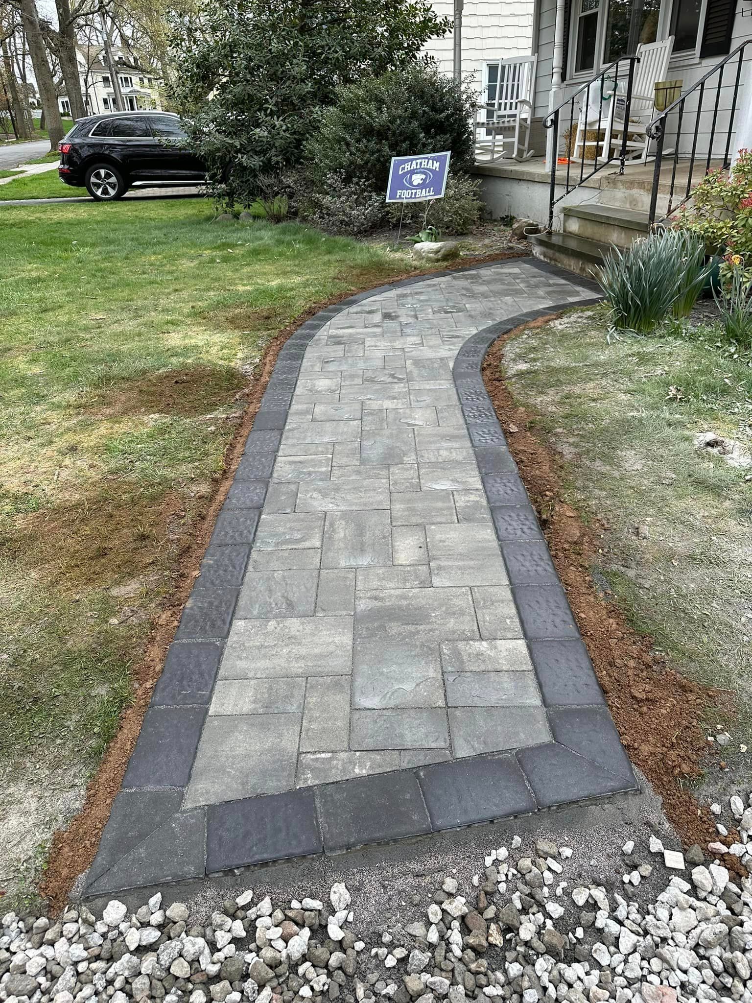 A brick walkway leading to a house with a car parked on the side of it.