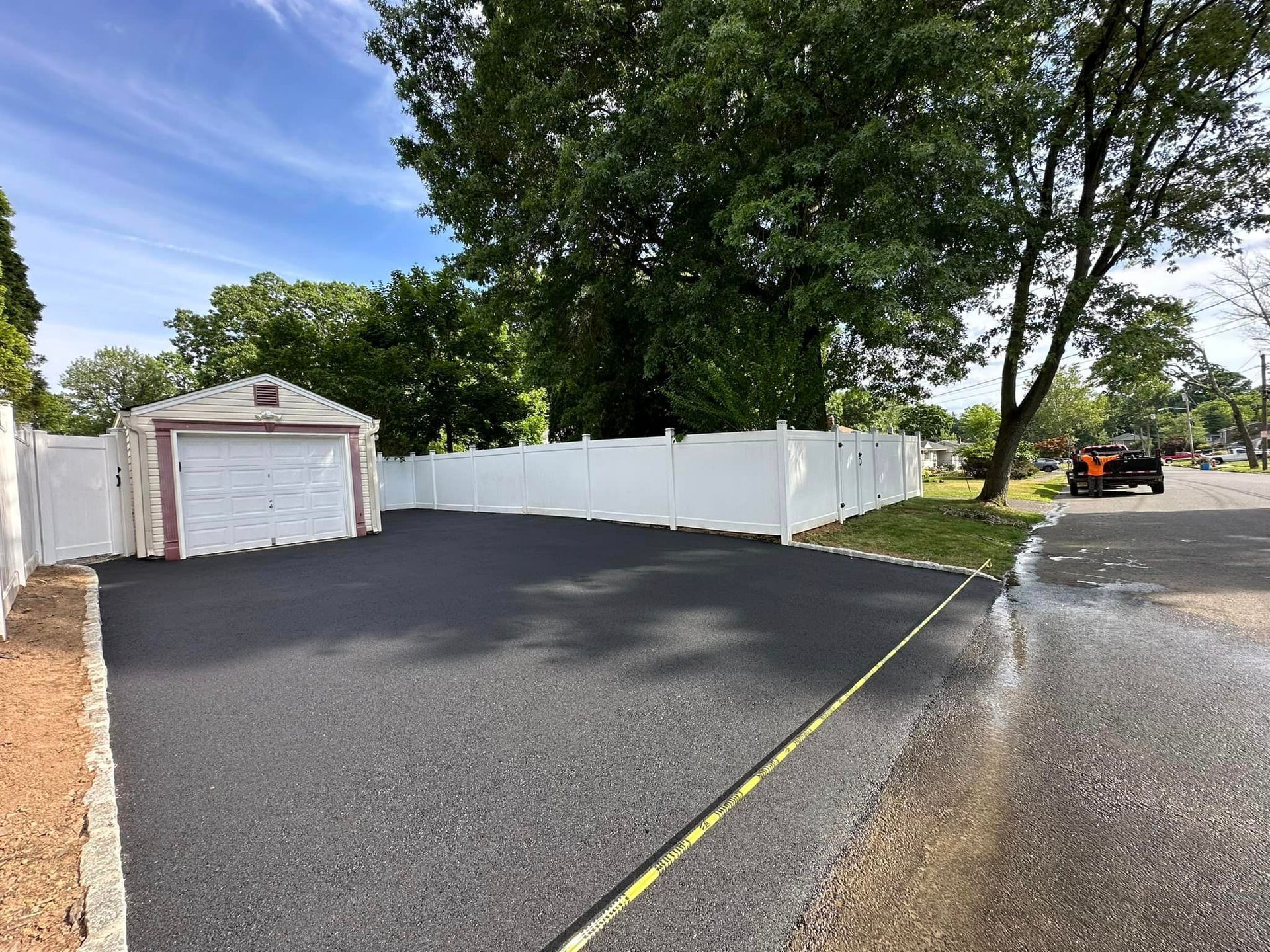 A driveway with a garage and a white fence.