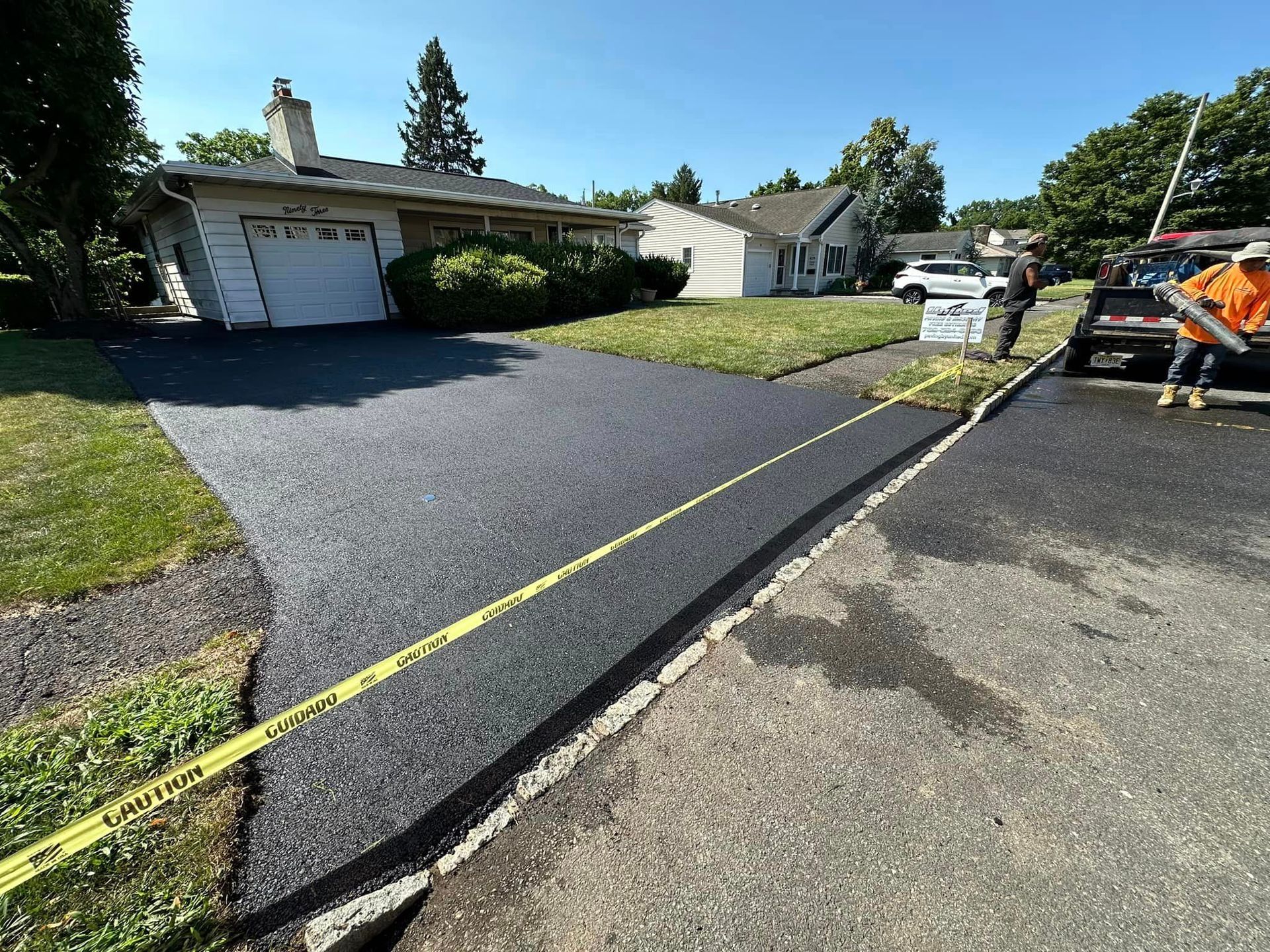 A man is laying asphalt in a driveway next to a house.