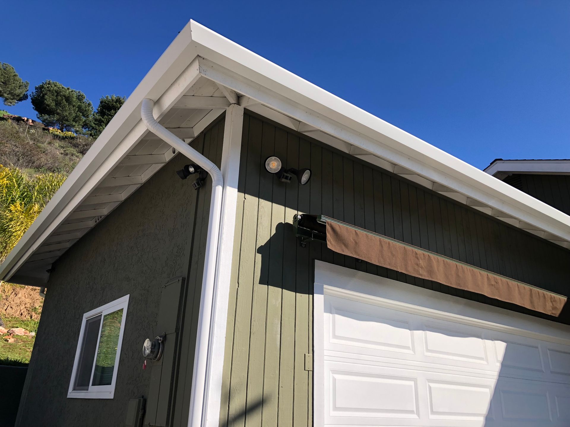 A green house with a white garage door and a white gutter