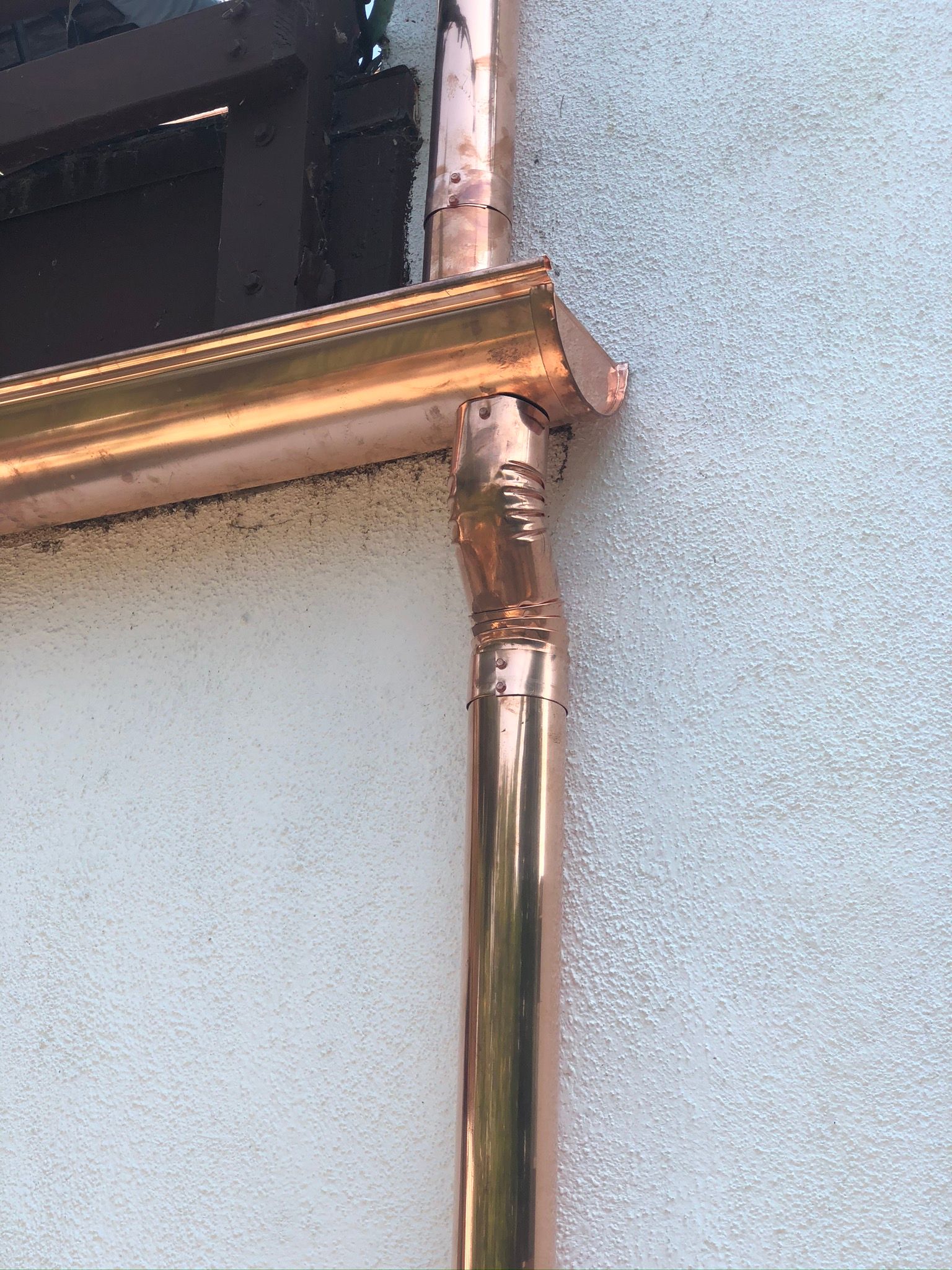 A close up of a copper pipe on the side of a building.