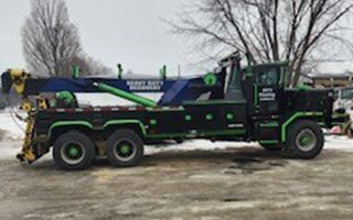 Black and green heavy duty tow truck on a snowy day.