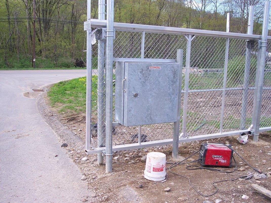 A metal box is sitting next to a chain link fence.