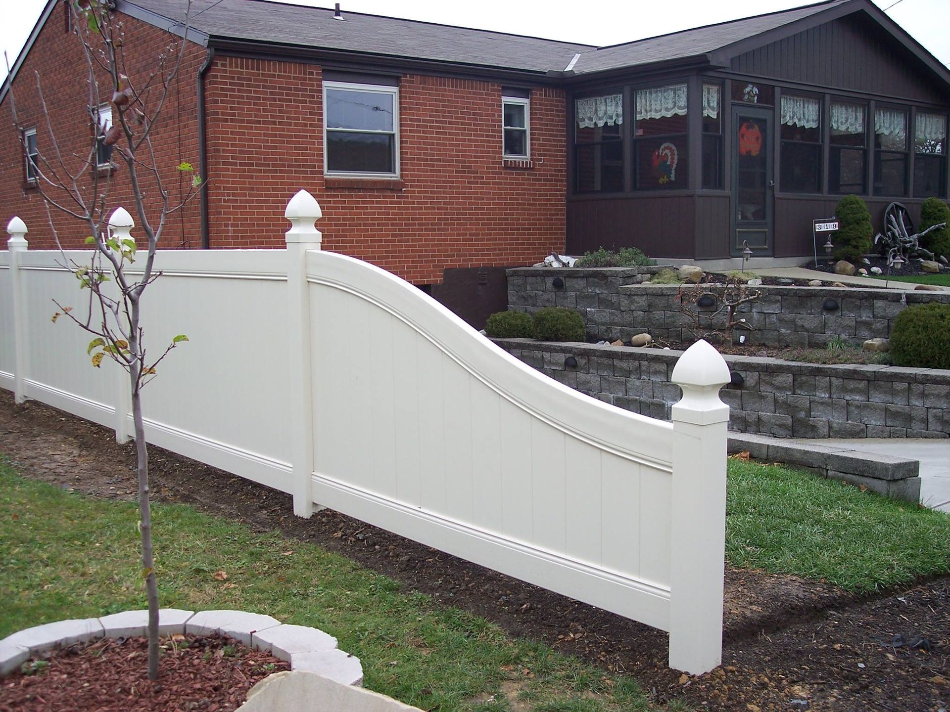 A white fence is in front of a brick house.