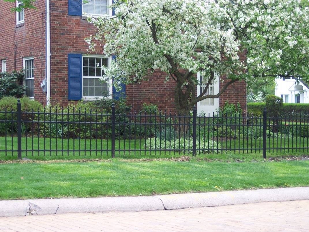 A black fence surrounds a lush green yard in front of a brick house.