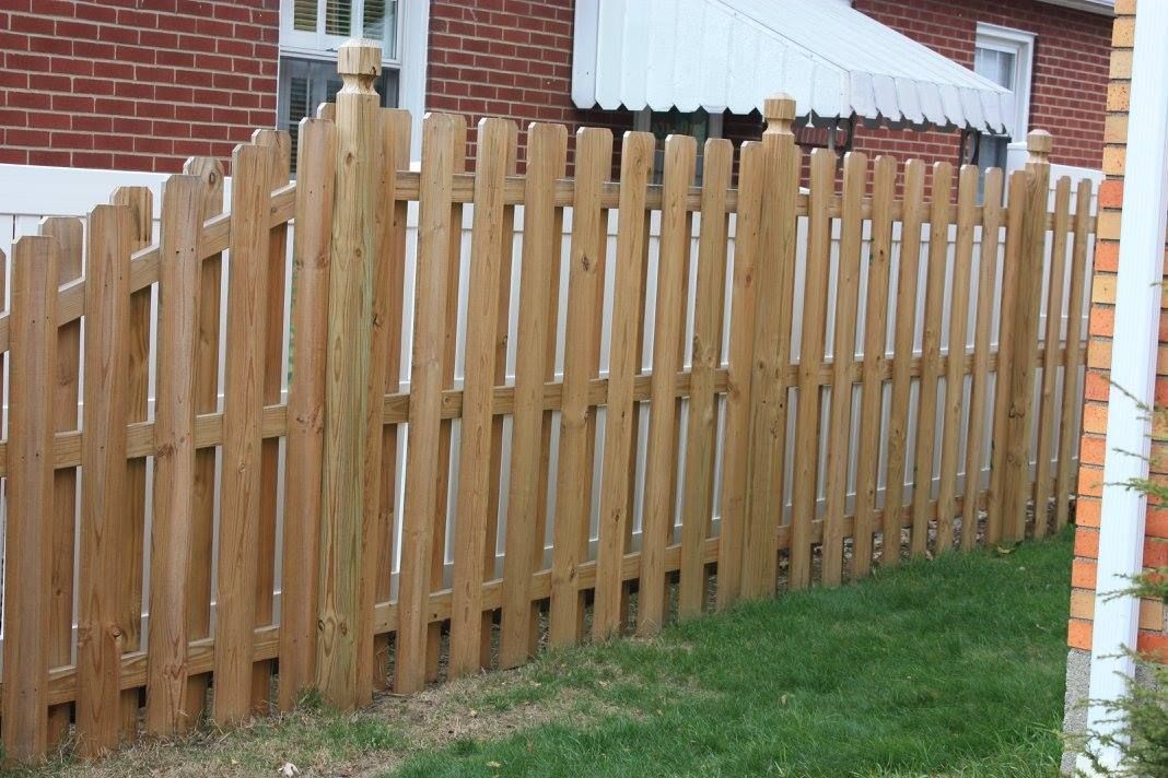 A wooden picket fence is in front of a brick building.