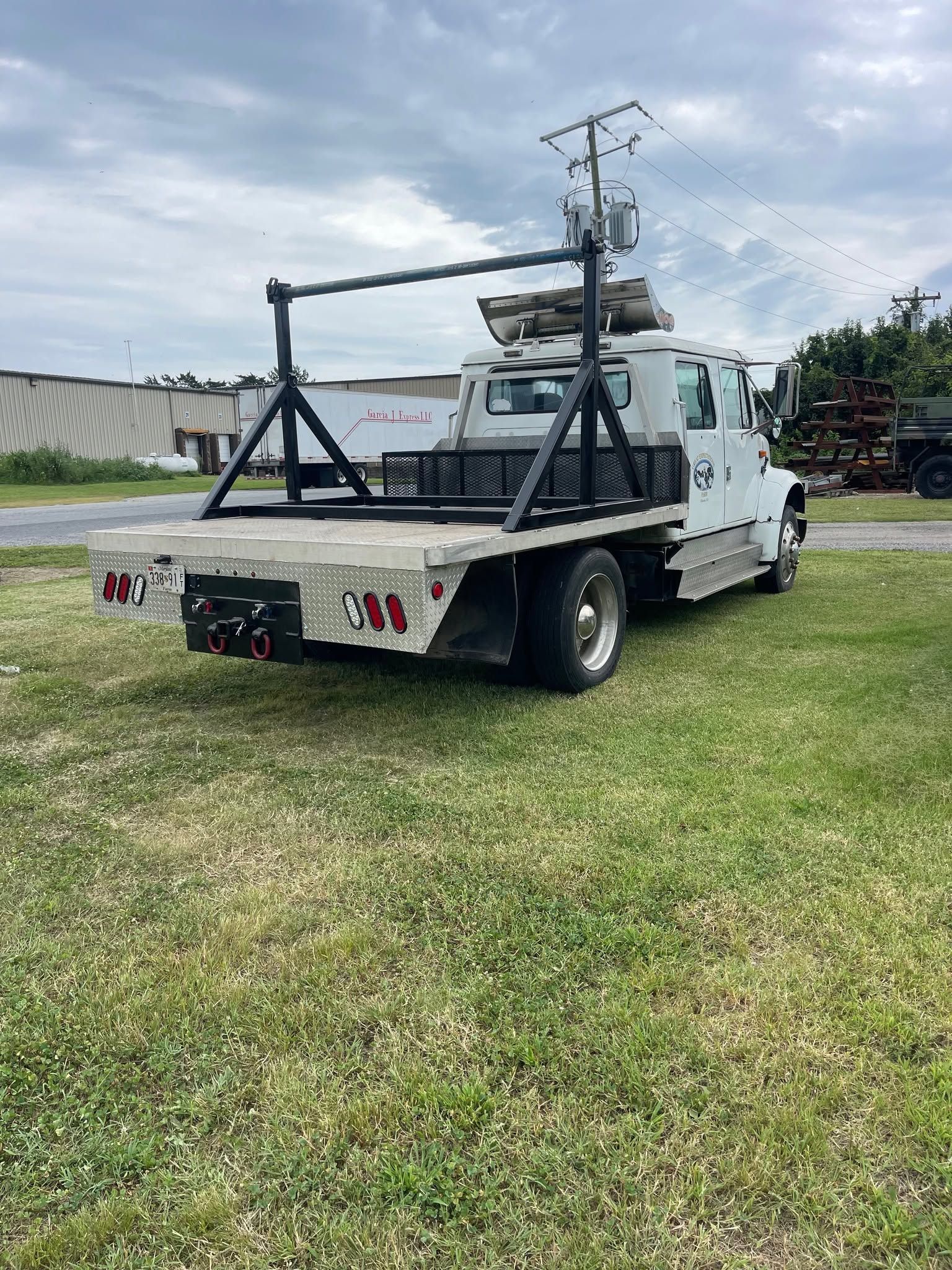White tow truck with rear crane parked on grass under a cloudy sky.