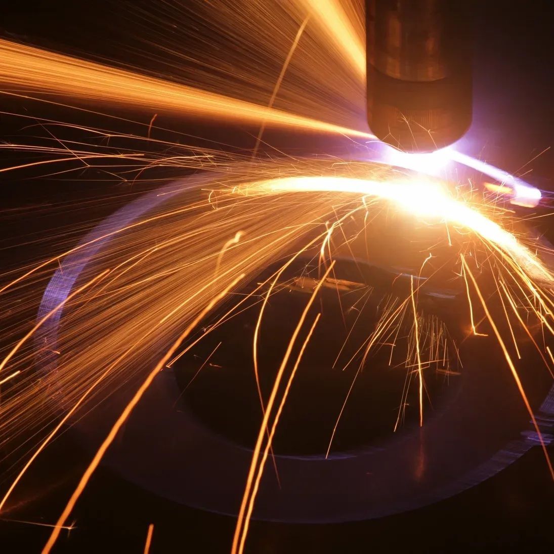 Close-up of a welding torch cutting metal, with bright sparks and orange light.