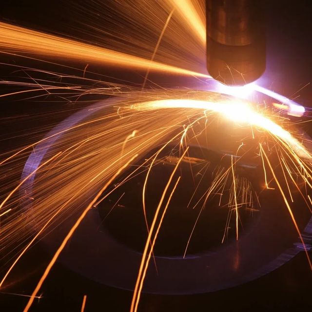 Close-up of a welding torch cutting metal, with bright sparks and orange light
