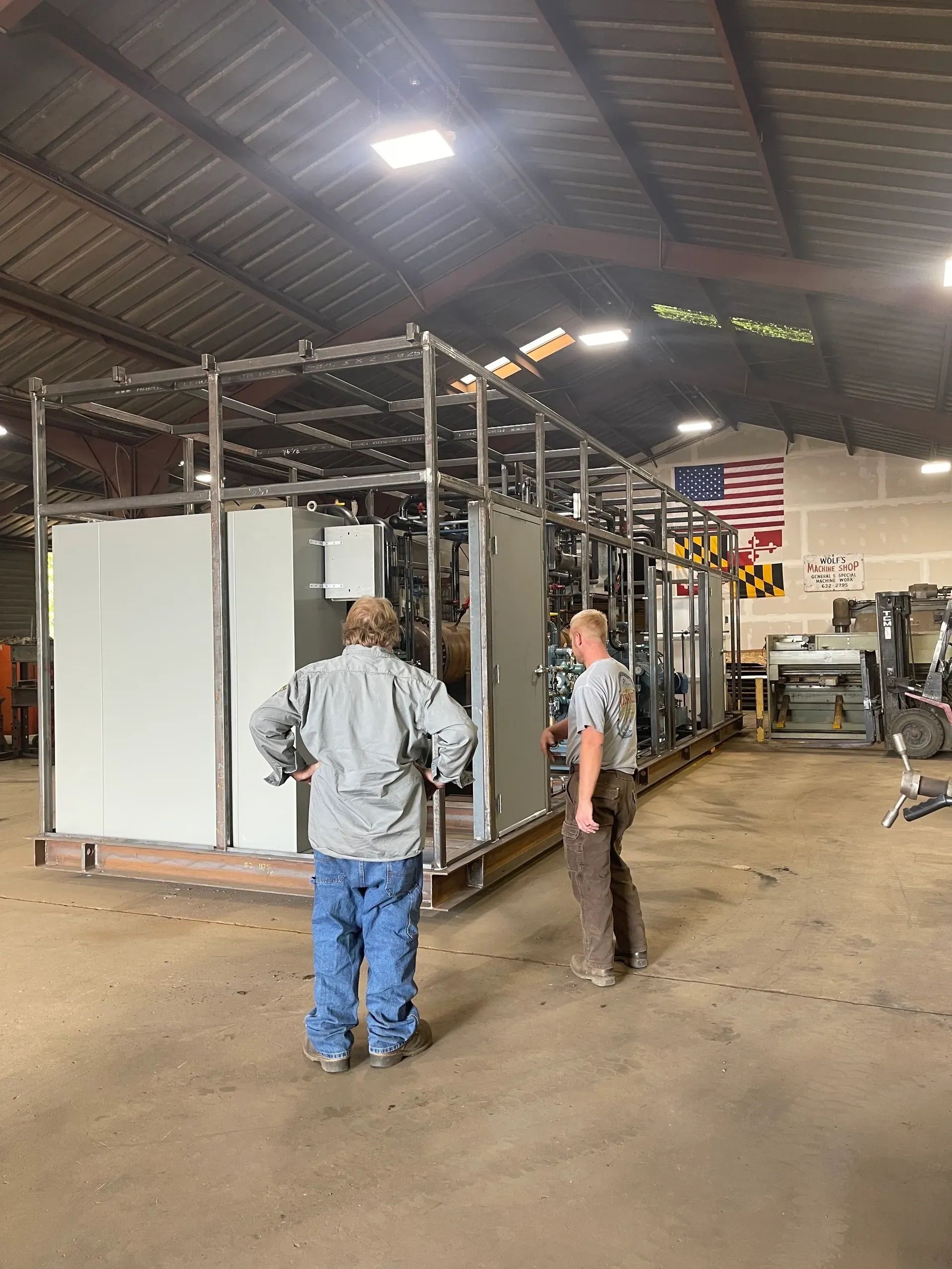 Two workers inspecting a metal industrial frame inside a warehouse workshop.