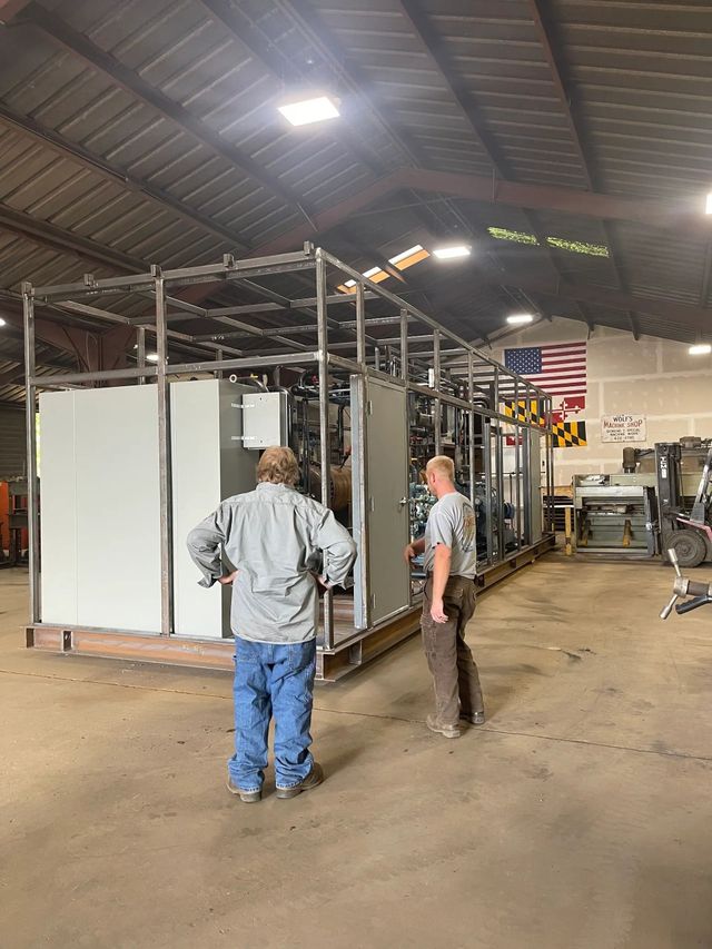 Two workers inspecting a metal industrial frame inside a warehouse workshop