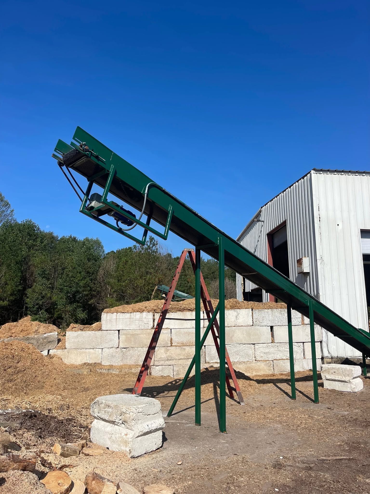 Green conveyor belt over a gravel pile beside a white industrial building under a blue sky.