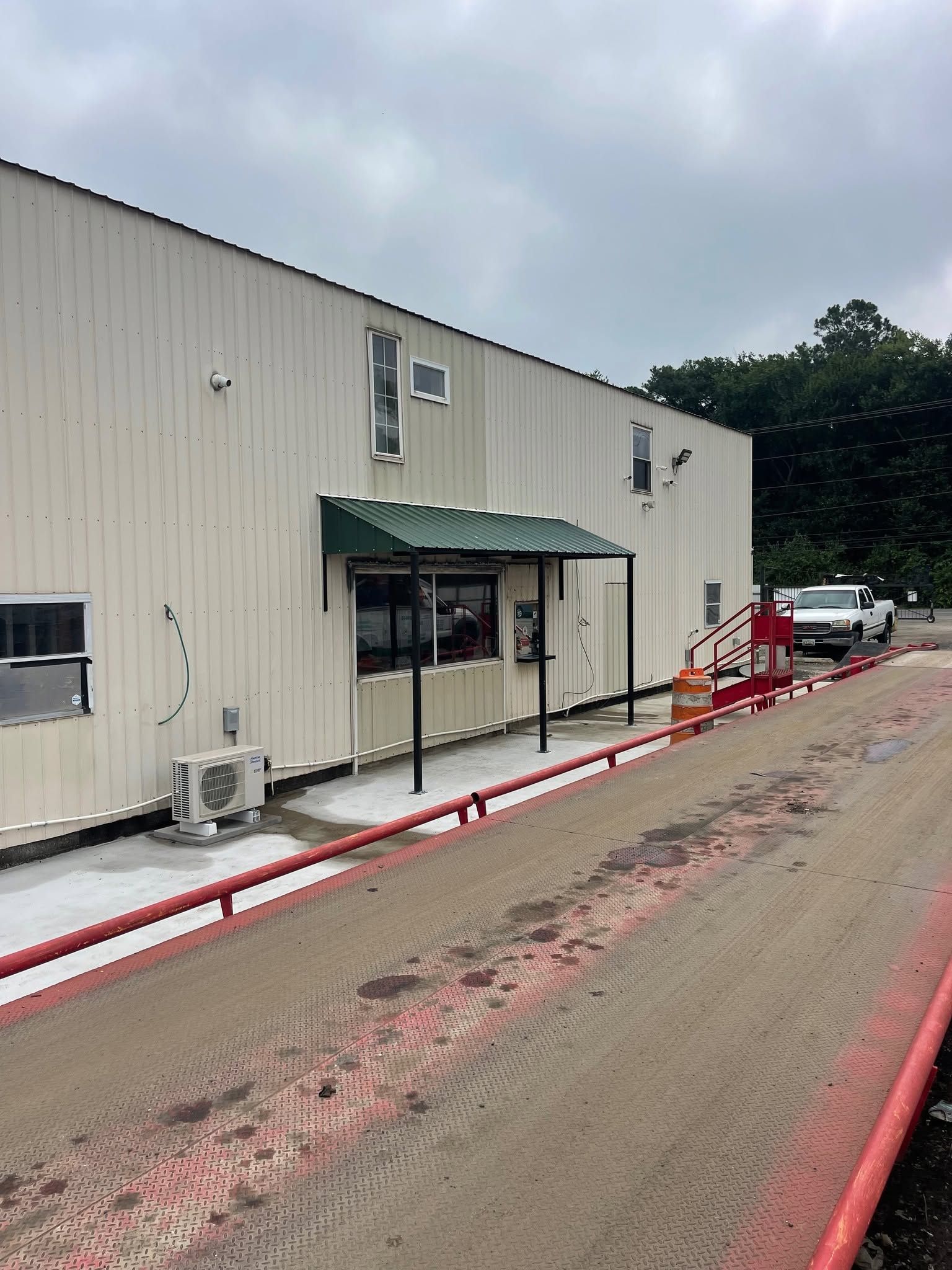 Industrial building with green awning and red hoses along a muddy road under cloudy skies.