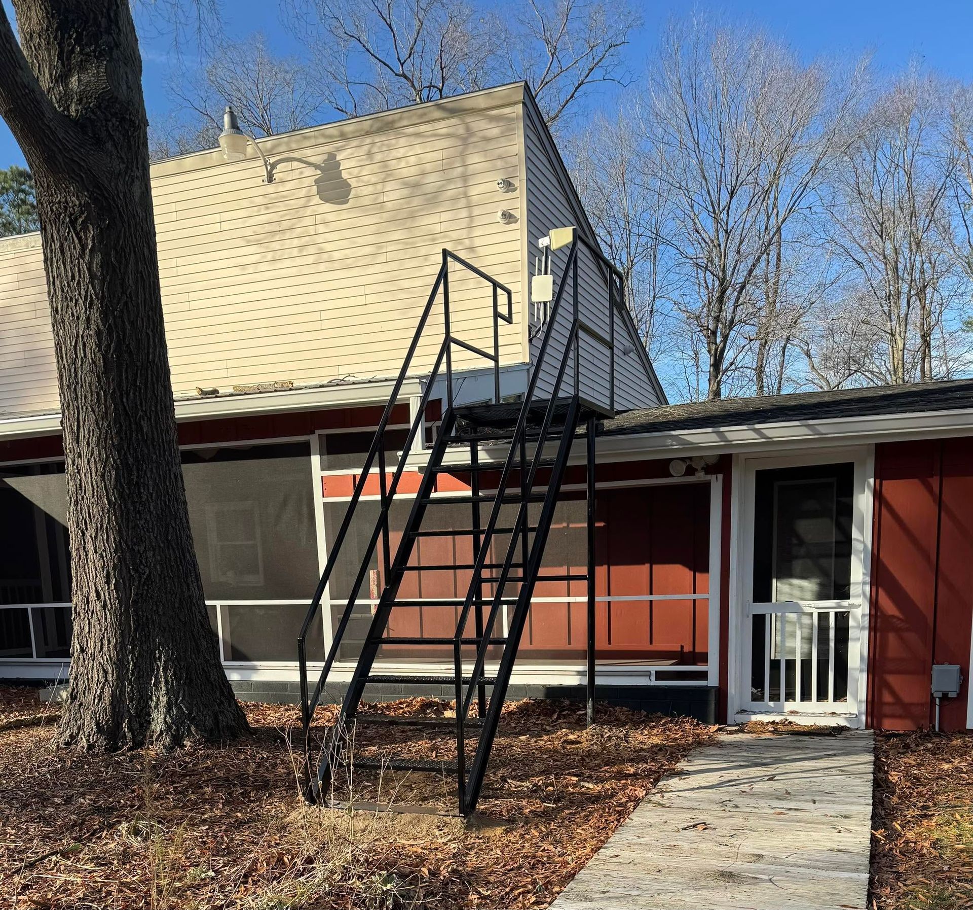 Outdoor metal staircase leaning against a red house beside a tree and walkway.
