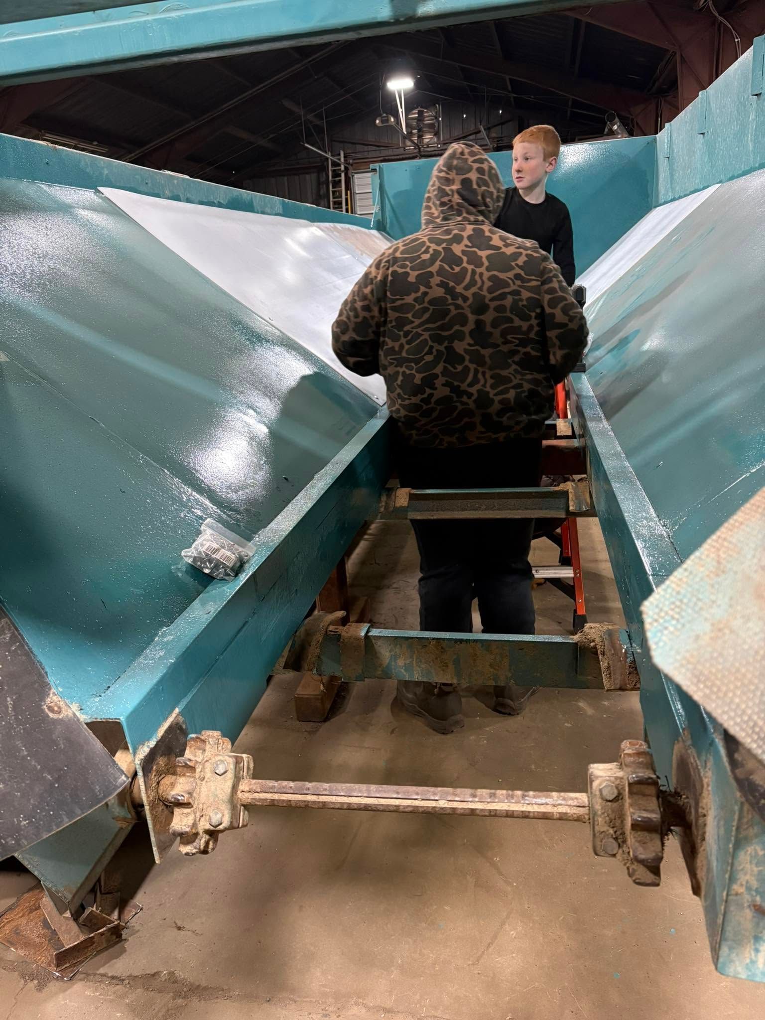 Person in camouflage jacket boards a ride cart inside a covered attraction, seen from behind.
