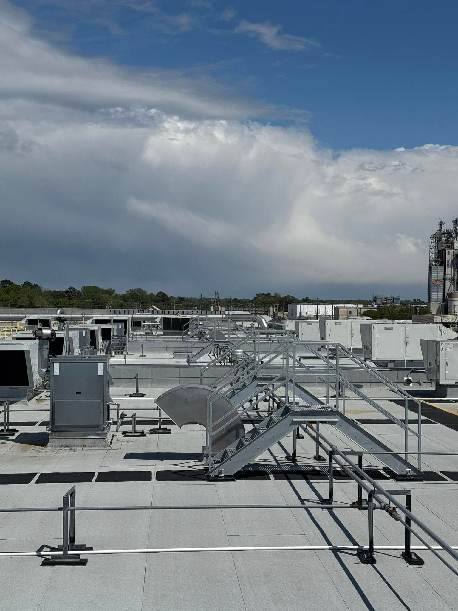 Rooftop HVAC units and metal catwalks under a cloudy blue sky.